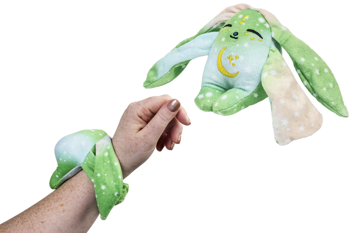 A person wears a green Clover Mini Wrist Hugger – Magnetic Sensory Plush while a matching bunny toy floats in the air nearby.