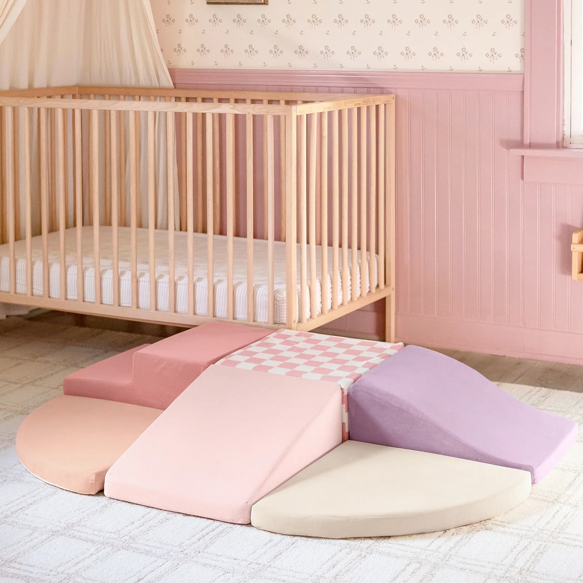 PlayNest Soft Foam Climbing Blocks – Violet include pastel shapes like ramps and steps, forming a toddler obstacle course on a nursery floor in front of a wooden crib.