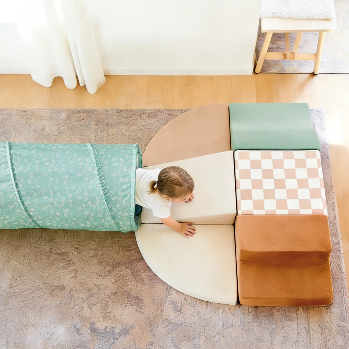 A toddler crawls out of a teal floral Adventure Crawl Tunnel (68″) onto a set of modular foam shapes in shades of tan, green, and brown.
