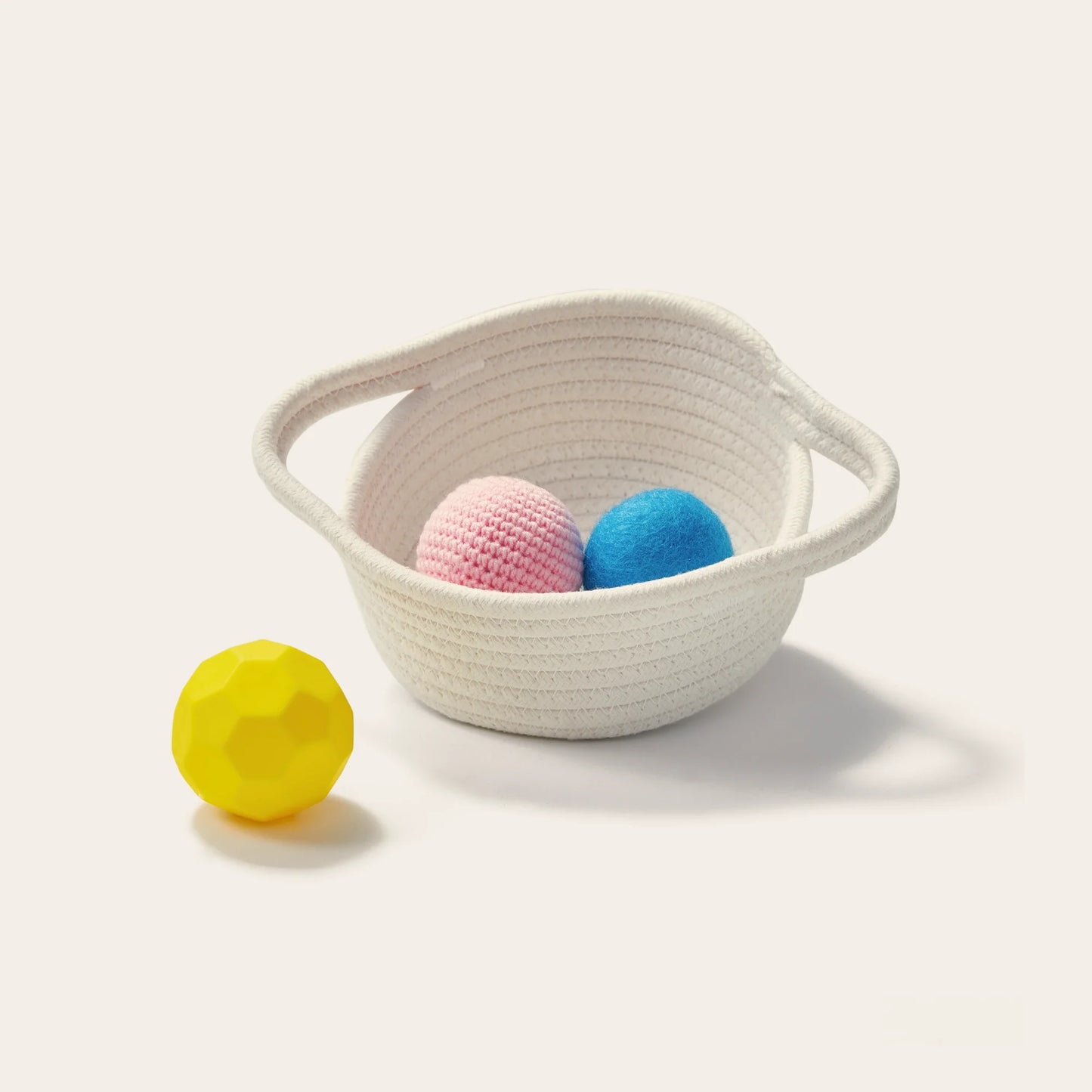 A Tiny Land® Montessori Toys for Newborns (7–9 Months) set is displayed: a white woven basket with pink and blue balls inside sits on a light surface, while a yellow sensory ball rests outside, creating a playful arrangement.