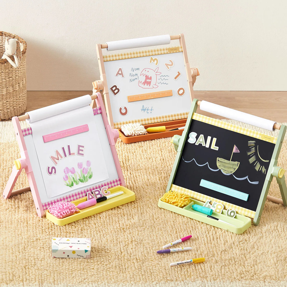 Three 3-in-1 Adjustable Tabletop Art Easels are arranged on a rug, each featuring a white surface with paper, a whiteboard, or a chalkboard with colorful artwork.