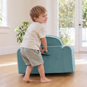 A young child standing behind and holding the handle of a teal foam GentleSnug Flip-Open Kids Sofa & Nap Mat.