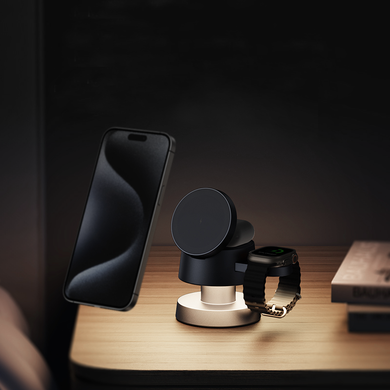 A smartphone and smartwatch sit on a modern 4-in-1 Wireless Charging Station atop a wooden bedside table next to two stacked books in a softly lit room, providing an ideal Apple device charging solution.