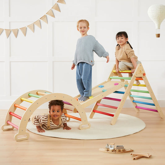 Three children play in a bright room with the Tiny Land® 7-in-1 Rainbow Climbing Set. One climbs the ramp, another crawls under the arch, and a third stands on a platform as colorful rungs and playful decor fill the scene.