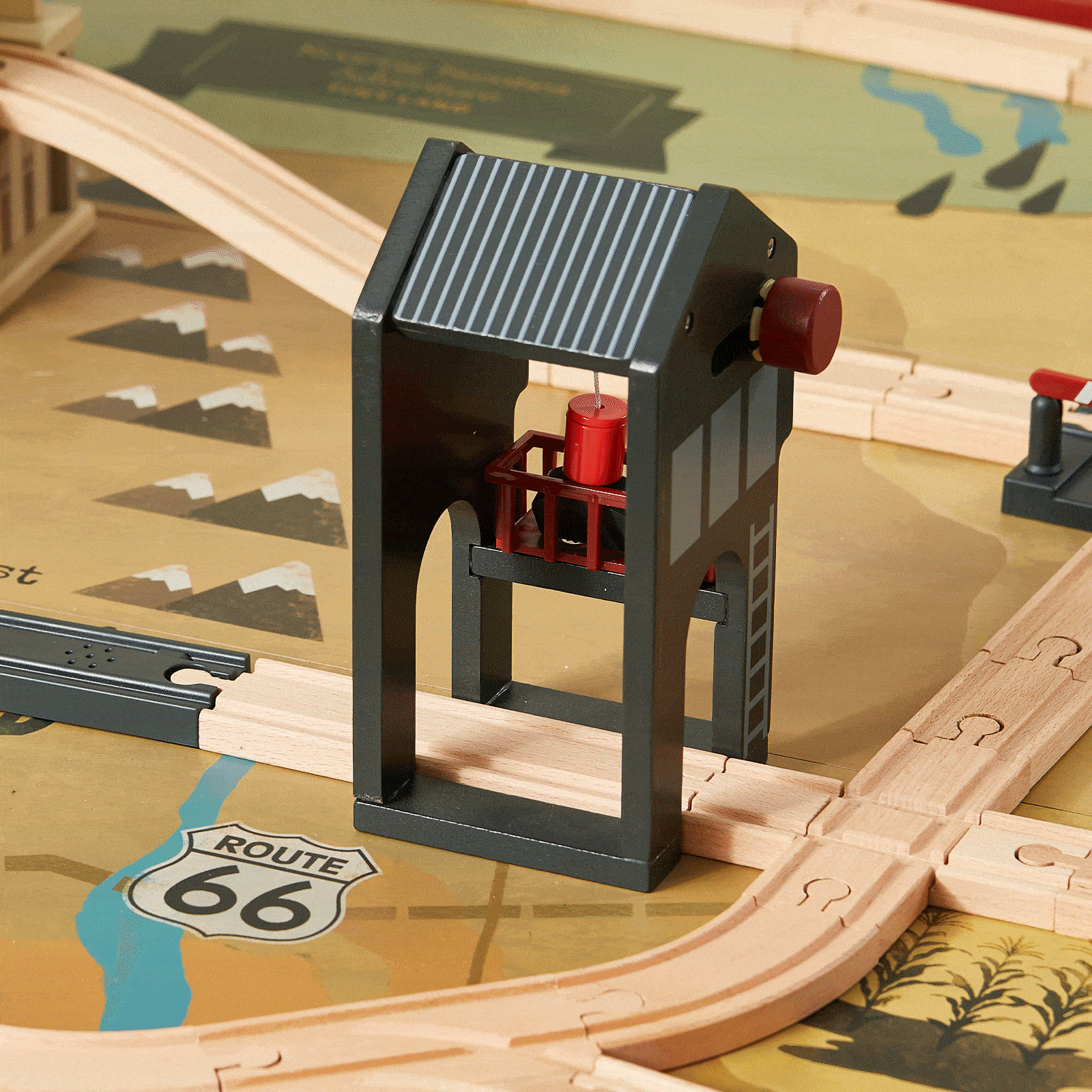 The 1920s Railway Wooden Train Table with Sounds features a wooden train track, black and red tower, Route 66 mat, illustrated mountains, and a vintage city scene.