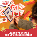 A person holds two ABC Uppercase & Lowercase Letters Card Pack flash cards showing the letter W, one with a walrus and the other with a watermelon, with a pile of cards and fidget toys on the table for letter recognition.