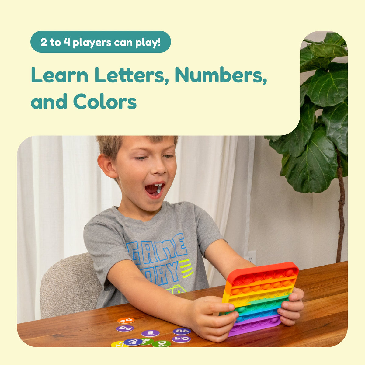 A young boy looks surprised while holding a colorful, square, dimpled fidget toy during an ABC BINGO! Letter Sounds Game session, with alphabet and number pieces spread out on the table for letter recognition.
