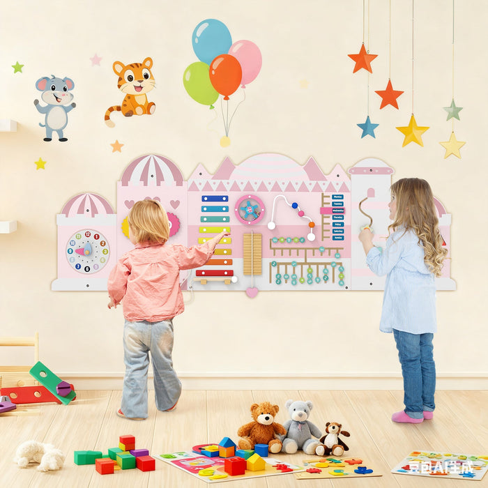 Two children play with an 11-in-1 Wooden Wall Busy Board – Pink Castle, featuring a clock, xylophone, gears, beads, and a calendar to support fine motor skills.