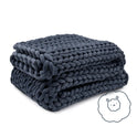A chunky, dark gray Ice Knit Weighted Blanket is folded neatly. In the bottom right corner, a small illustration of a smiling sheep in a fluffy cloud hints at this breathable blanket’s cozy comfort.