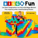 A smiling child stands in a colorful house made from Jumbo Building Blocks 36 PC with 3 Wheel Kits - Train Set, featuring easy stacking and soft edges for safe, creative play.