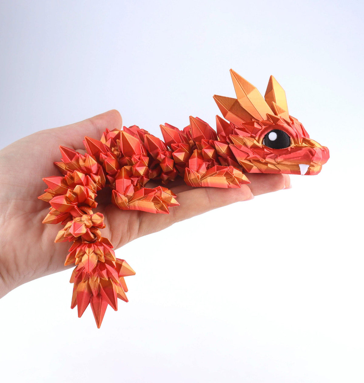 A person holds a shimmering, orange and red Crystal Baby Dragon – Poseable Fidget Toy with a faceted, crystalline appearance.