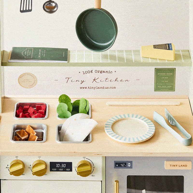 A BistroSwitch 2-in-1 Play Kitchen & Bistro wooden play kitchen featuring a stovetop with four inset bins of toy food, a striped plate, tongs, and a digital-style oven display for immersive role-play.