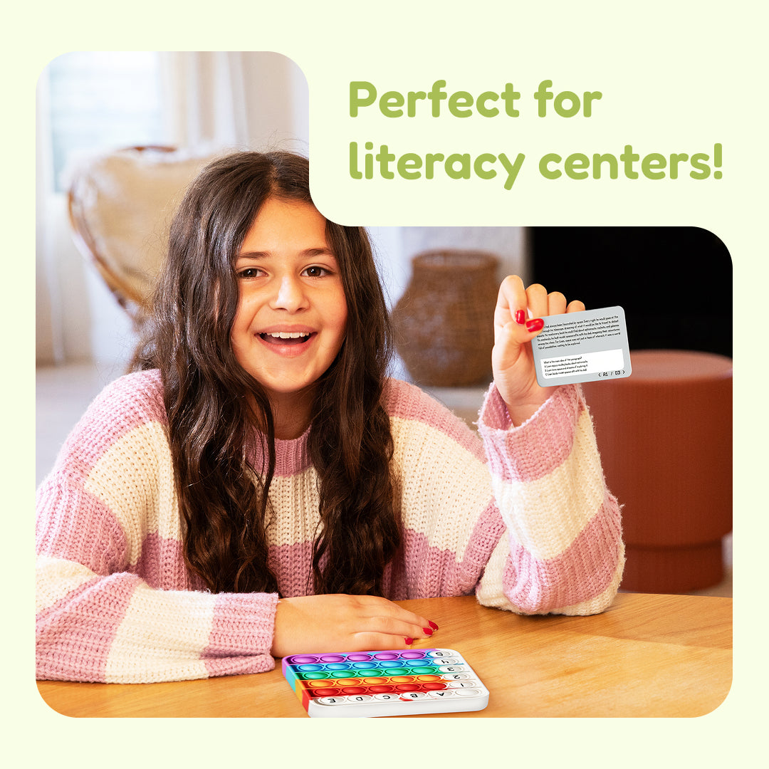 A smiling girl holds a Comprehension Codes Reading Game card while a colorful, alphabet-labeled fidget toy sits on the table.