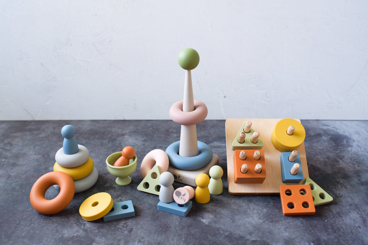 The Montessori Sensory Starter Kit – 3 Toy Set includes a stacking ring tower, a peg board with geometric shapes, and a nesting cup with a ball to encourage fine motor skills.