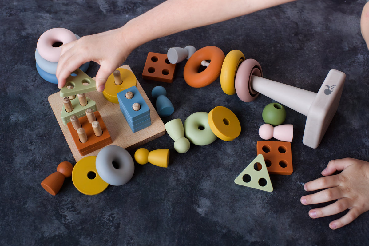 A child’s hands playing with a Montessori Sensory Starter Kit – 3 Toy Set, featuring wooden geometric shapes and pegs in assorted colors to develop fine motor skills.