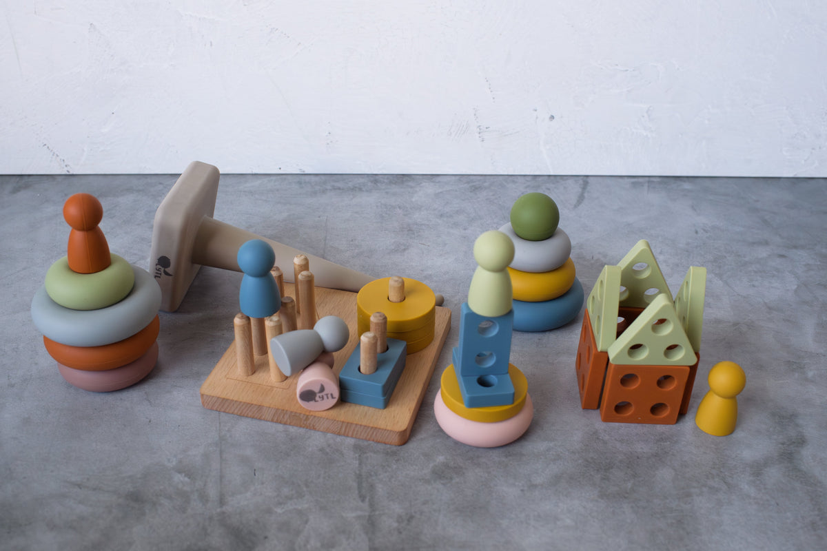 Montessori Sensory Starter Kit – 3 Toy Set including a stacking ring tower, a peg board with silicone peg dolls, a stacking toy with a spherical topper, and a house-shaped block structure.