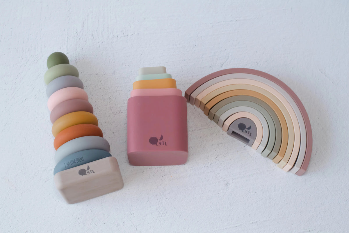 The Stack Happy Trio – Montessori Stacking Set features a stacking ring tower, a set of nesting blocks, and a rainbow stacker in muted, earthy tones designed for sensory play.