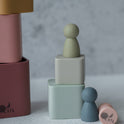 Two Silicone Mini Peg Dolls (Set of 6) perched on stacked silicone blocks, with additional blocks and a peg doll lying nearby as travel toys.