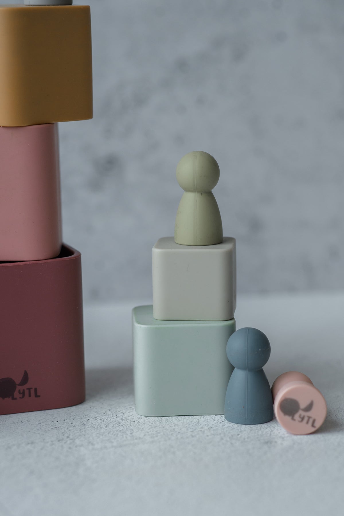 Two Silicone Mini Peg Dolls (Set of 6) perched on stacked silicone blocks, with additional blocks and a peg doll lying nearby as travel toys.