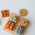 Montessori Wood & Silicone Shape Puzzle featuring a wooden base with upright pegs and muted silicone geometric shapes designed to support baby’s fine motor skills.