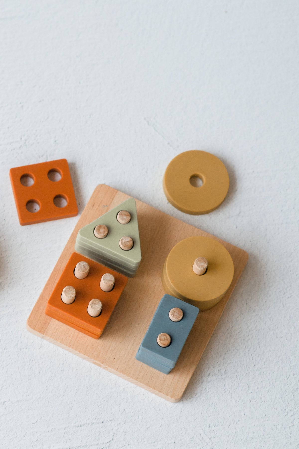 Montessori Wood & Silicone Shape Puzzle featuring a wooden base with upright pegs and muted silicone geometric shapes designed to support baby’s fine motor skills.