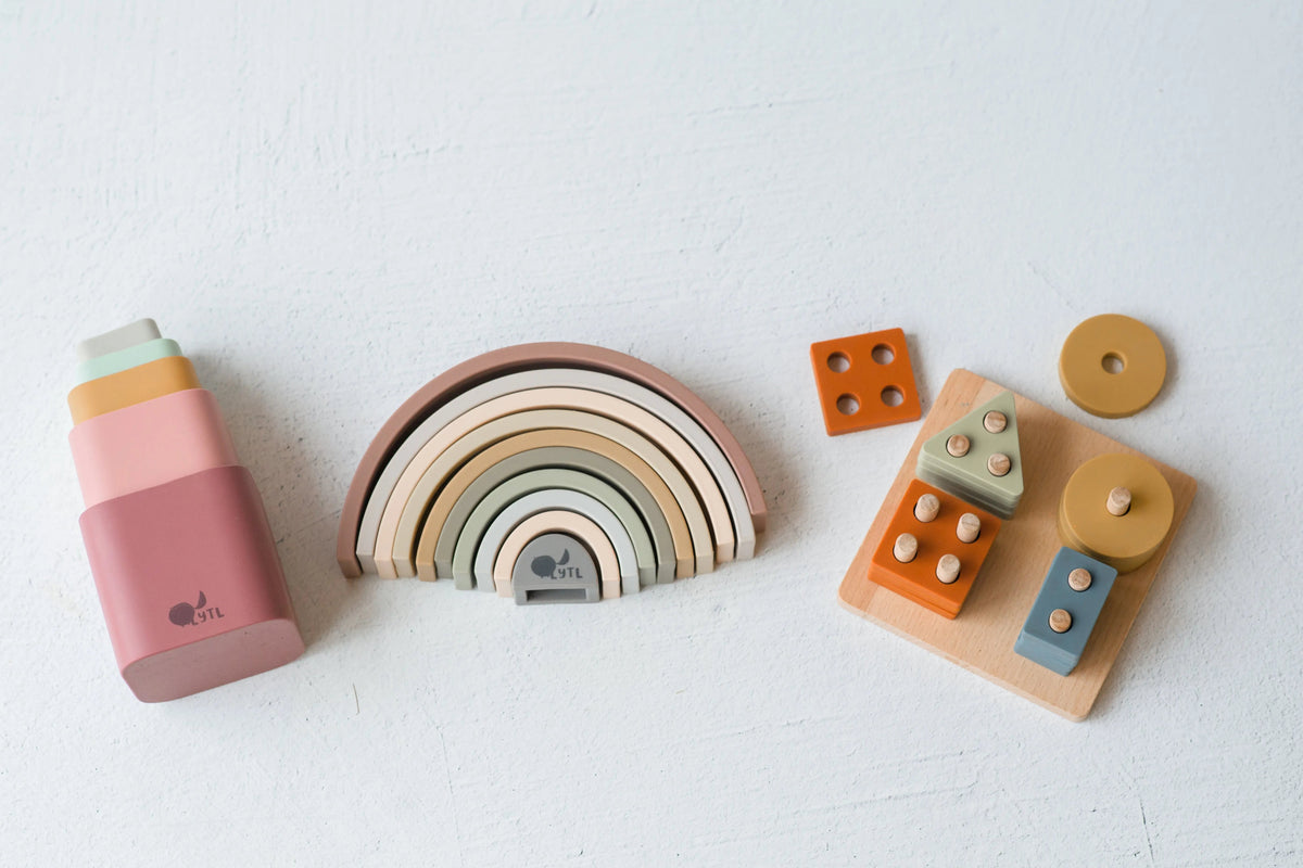 Silicone Stacking Cups (Set of 5), a rainbow stacker toy, and a wooden shape sorting board with various colored geometric blocks.