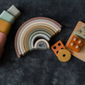 Silicone Stacking Cups (Set of 5), a nested rainbow-shaped stacking toy, and a wooden shape-sorting board with various blocks arranged on a dark surface.
