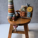 A wooden stool holding the Montessori Fine Motor Play Bundle – 3 Toys, which includes Montessori stacking toys, a shape-sorting board, and several mushroom-shaped toys.