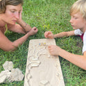 An adult and a child sitting in the grass, assembling The Oort Cloud – Wooden Marble Run Puzzle on a board.