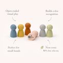Six colorful, smooth Silicone Mini Peg Dolls (Set of 6) arranged on a white surface, with text annotations highlighting features like color recognition and their suitability as travel toys for small hands.