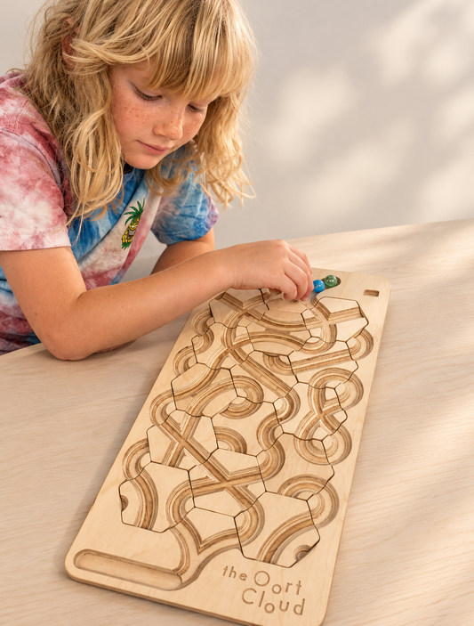 A child places a marble onto The Oort Cloud – Wooden Marble Run Puzzle, which features interlocking tracks.