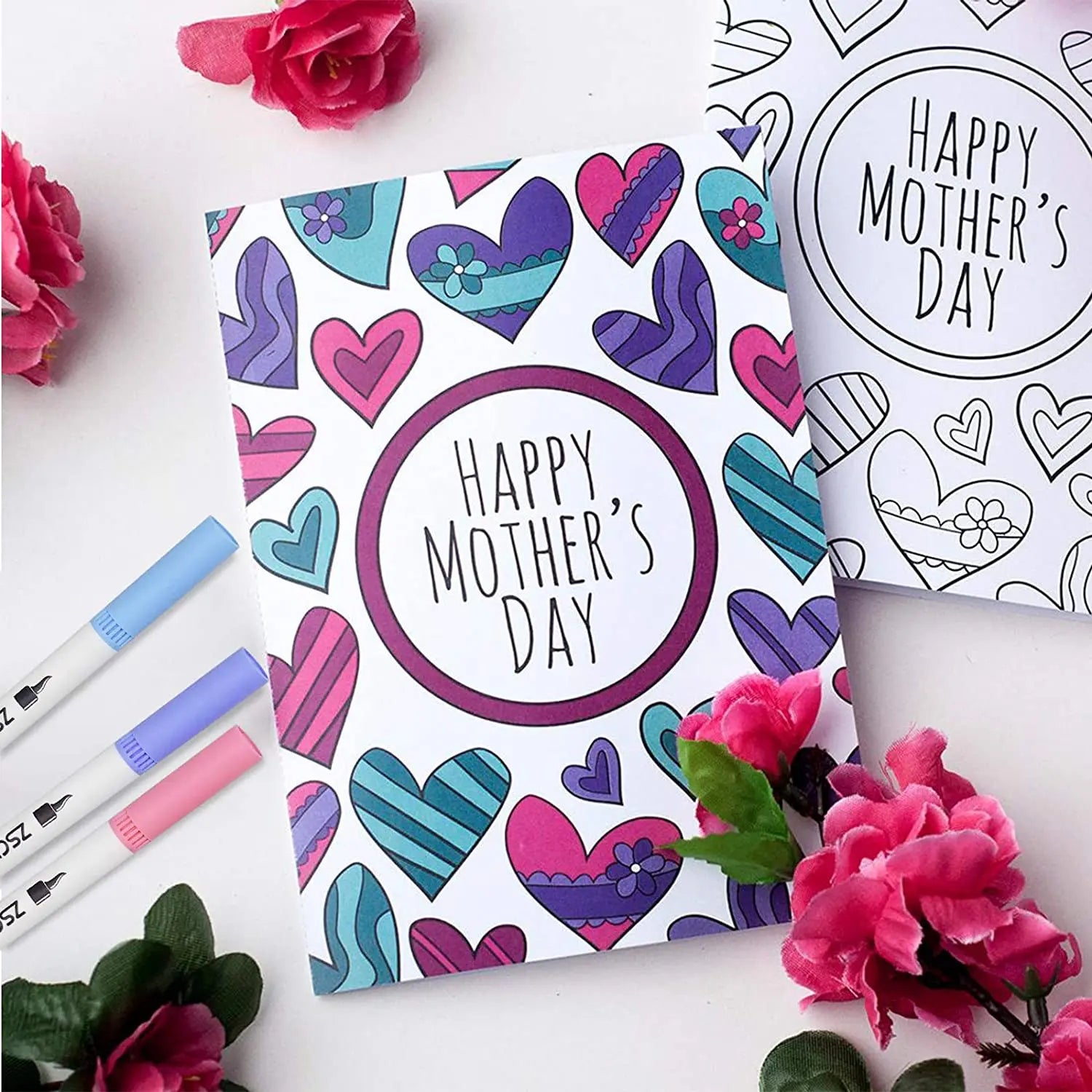A Mothers Day card with vibrant hearts is surrounded by pink flowers and the Vibrant Dual Tip Brush Pen Marker Set, which offers 12 to 160 colors for creative drawing, coloring, and sketching.