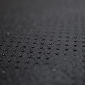 Close-up of the Desk Mat Bundle in textured black vegan leather, featuring small, evenly spaced raised dots in a grid pattern and an ergonomic wrist cushion, shot with a shallow depth of field and a softly blurred background.