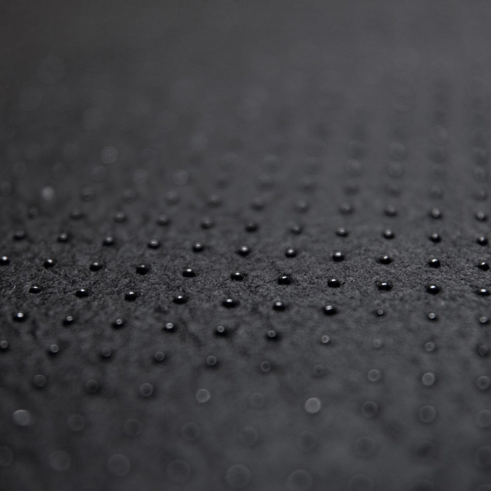 Close-up of the Desk Mat Bundle in textured black vegan leather, featuring small, evenly spaced raised dots in a grid pattern and an ergonomic wrist cushion, shot with a shallow depth of field and a softly blurred background.