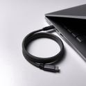 A Magnetic Charging Cable is coiled next to a sleek, partially open laptop on a white surface. The cable is connected to one of the laptop’s ports.