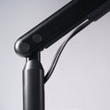 Close-up of a black adjustable Single Monitor Arm with visible cables, set against a light gray background—ideal for enhancing your ergonomic workspace or pairing seamlessly with your monitor setup.