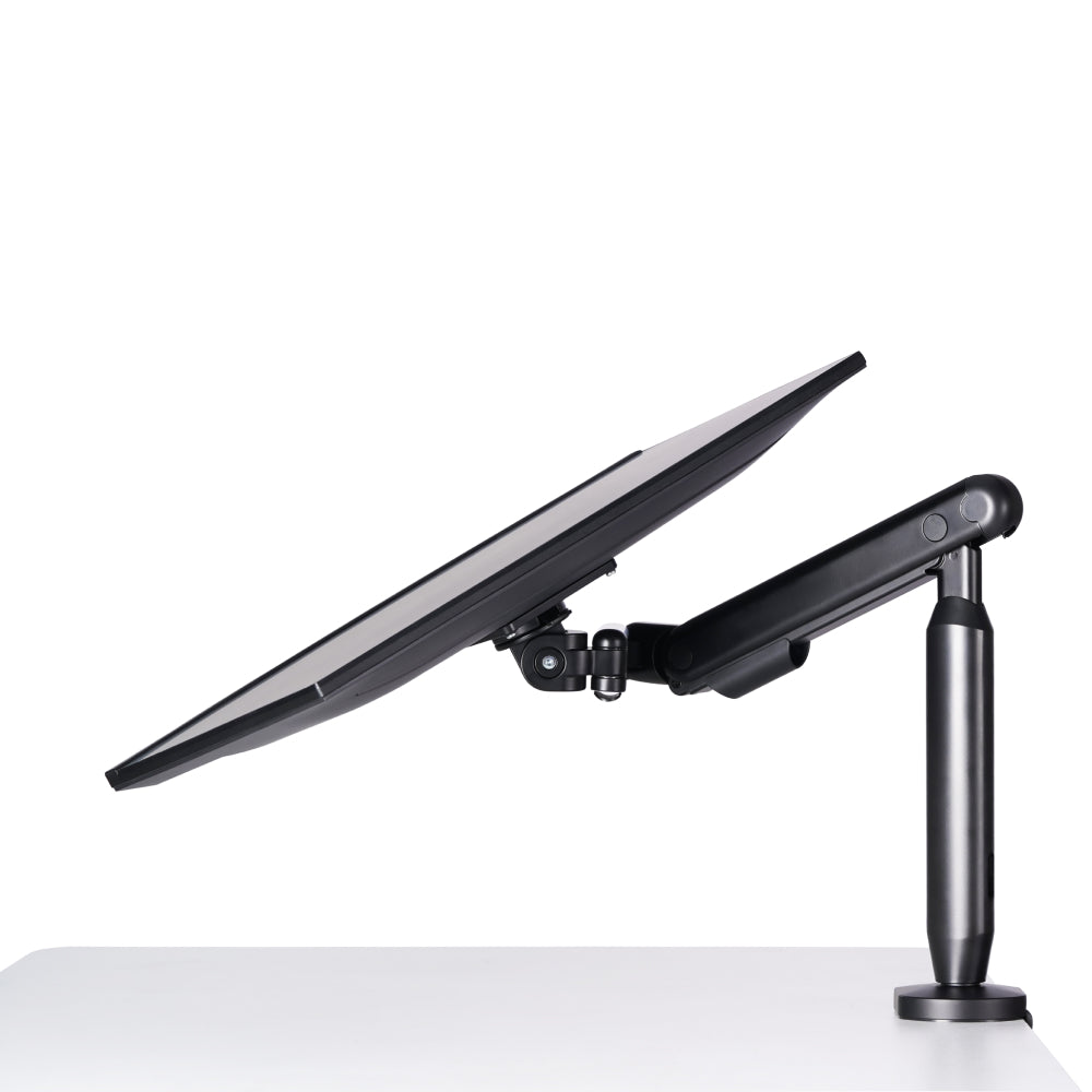 A Single Monitor Arm supports a computer monitor at a low, angled tilt above a white desk, displaying the side view of both the monitor and mounting arm for an ergonomic workspace.