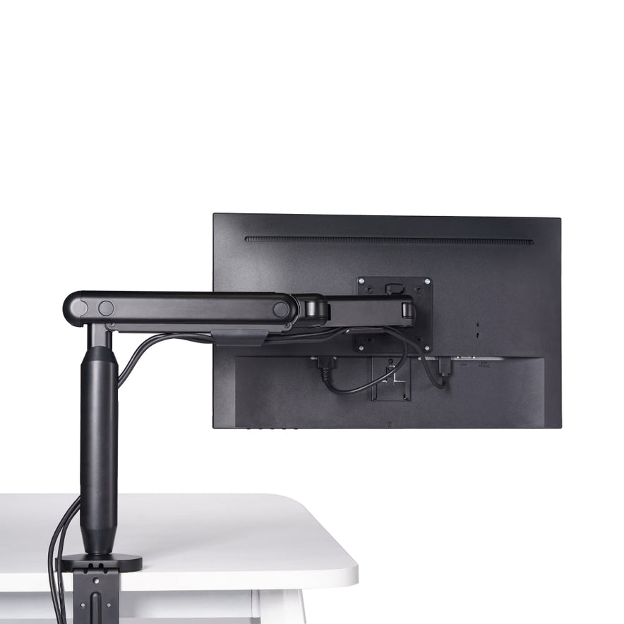 The Single Monitor Arm, in black, is mounted on a white desk and supports a flat-screen monitor. Its sleek design keeps cables organized for an ergonomic workspace, all set against a plain white background.