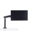 A black Single Monitor Arm holds a computer monitor at the edge of a white desk, creating an ergonomic workspace against a plain white background.