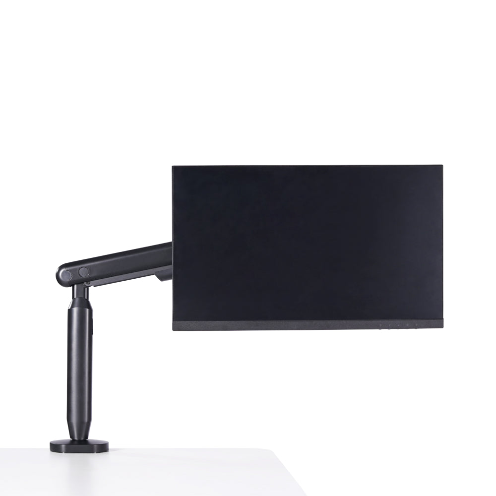 A black Single Monitor Arm holds a computer monitor at the edge of a white desk, creating an ergonomic workspace against a plain white background.