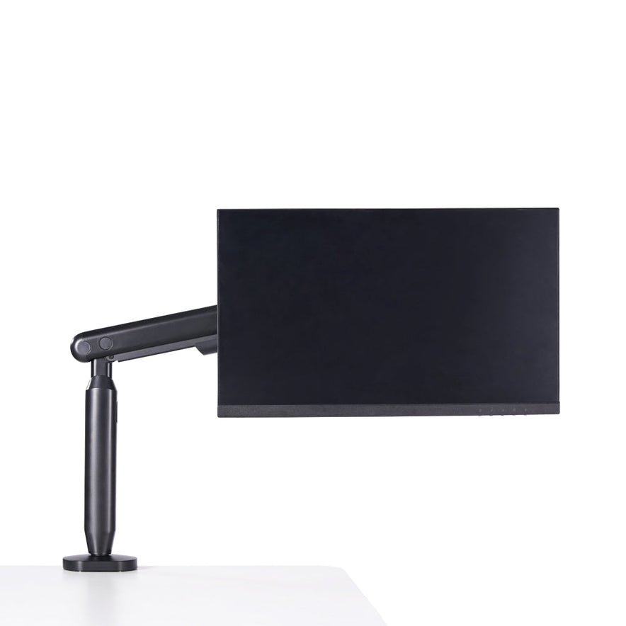 A black Single Monitor Arm holds a computer monitor at the edge of a white desk, creating an ergonomic workspace against a plain white background.