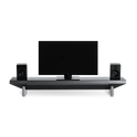 The Hexcal Studio™ is a modern home entertainment setup with a flat-screen TV, black speakers, and a sleek soundbar shelf with metallic legs and built-in cable management, all shown against a plain white background.