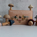 A Mushroom Mix & Match Sorting Toy (24 pc) set featuring color sorting mushrooms with wooden stems and silicone caps arranged around their cardboard packaging.