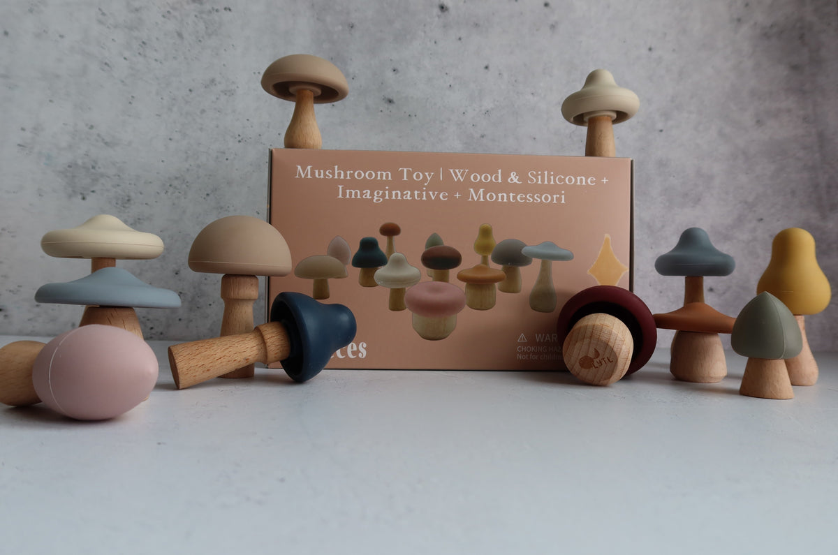 A Mushroom Mix & Match Sorting Toy (24 pc) set featuring color sorting mushrooms with wooden stems and silicone caps arranged around their cardboard packaging.