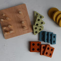 The Montessori Wood & Silicone Shape Puzzle is a wooden shape sorter with pegs next to groups of yellow circles, olive triangles, blue rectangles, and rust-colored squares, designed to help children develop fine motor skills.