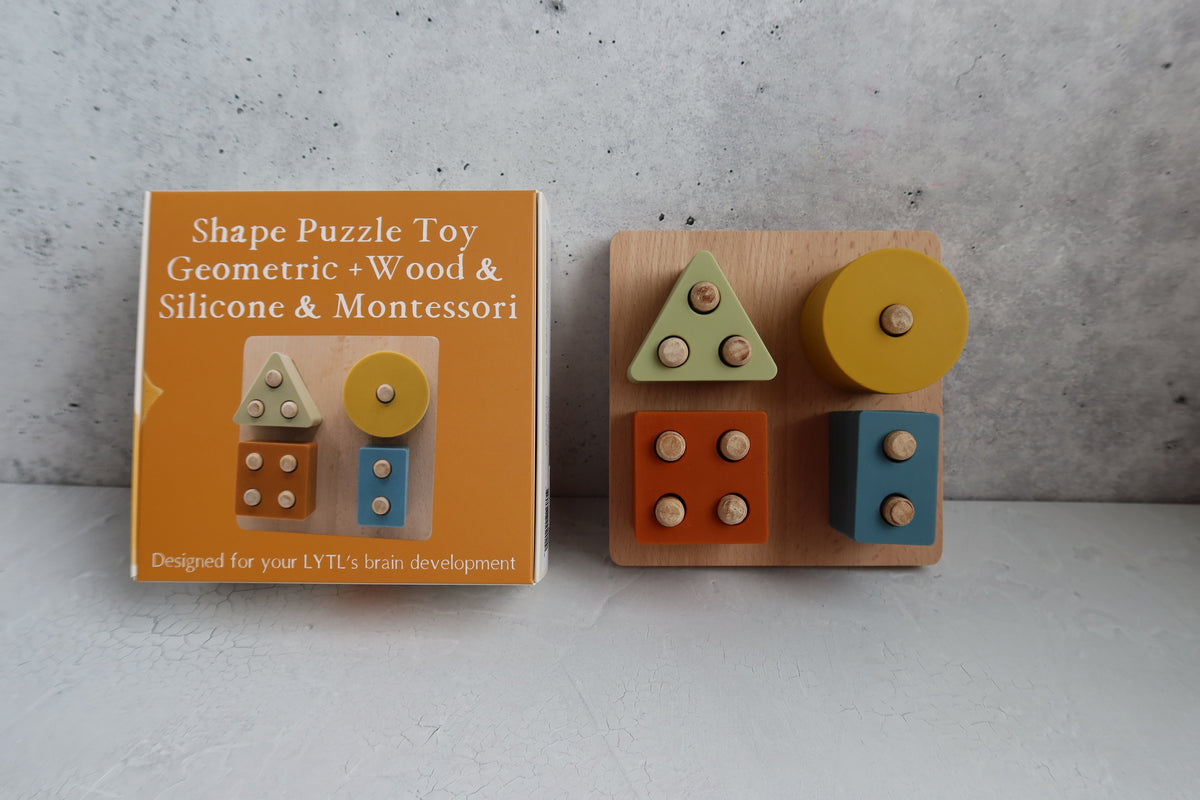 A Montessori Wood & Silicone Shape Puzzle consisting of a square wooden shape sorter with four geometric pieces and its corresponding orange cardboard box.