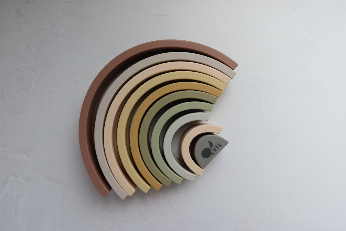 Silicone Rainbow Stacking Toy (10 pc) featuring ten nested silicone arches in graduated muted earth tones.