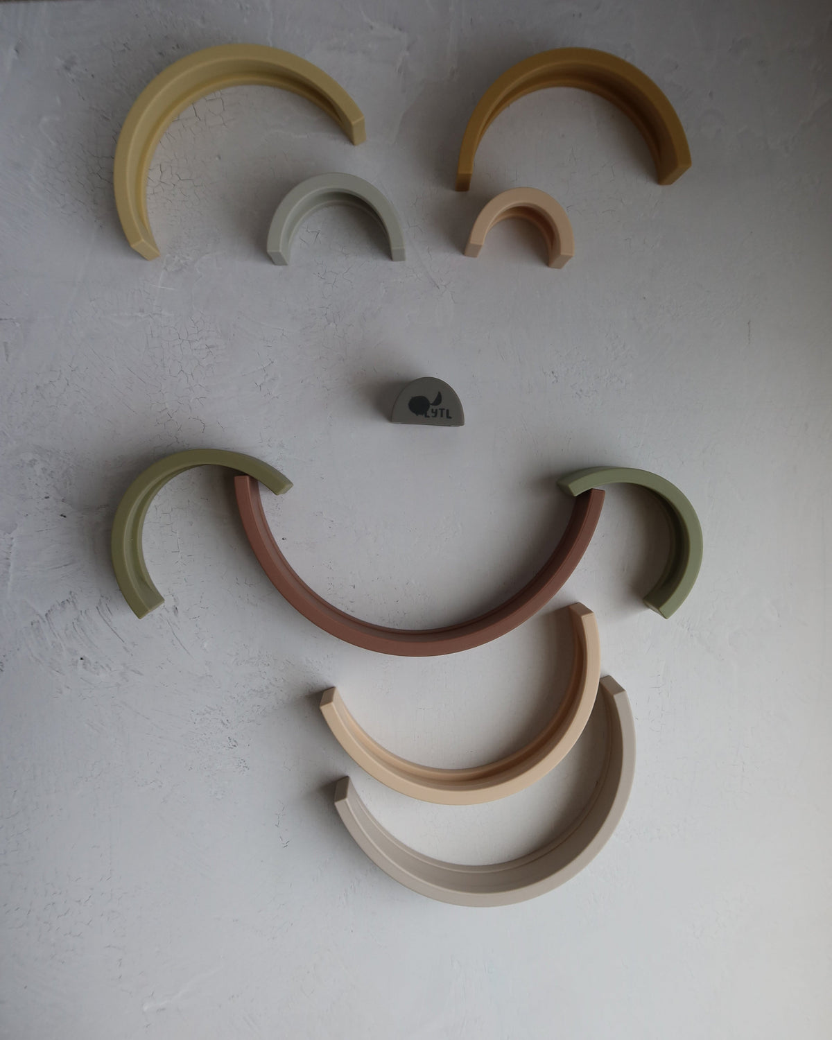 Ten pieces of the Silicone Rainbow Stacking Toy (10 pc) arranged in a smiley face pattern on a textured surface.