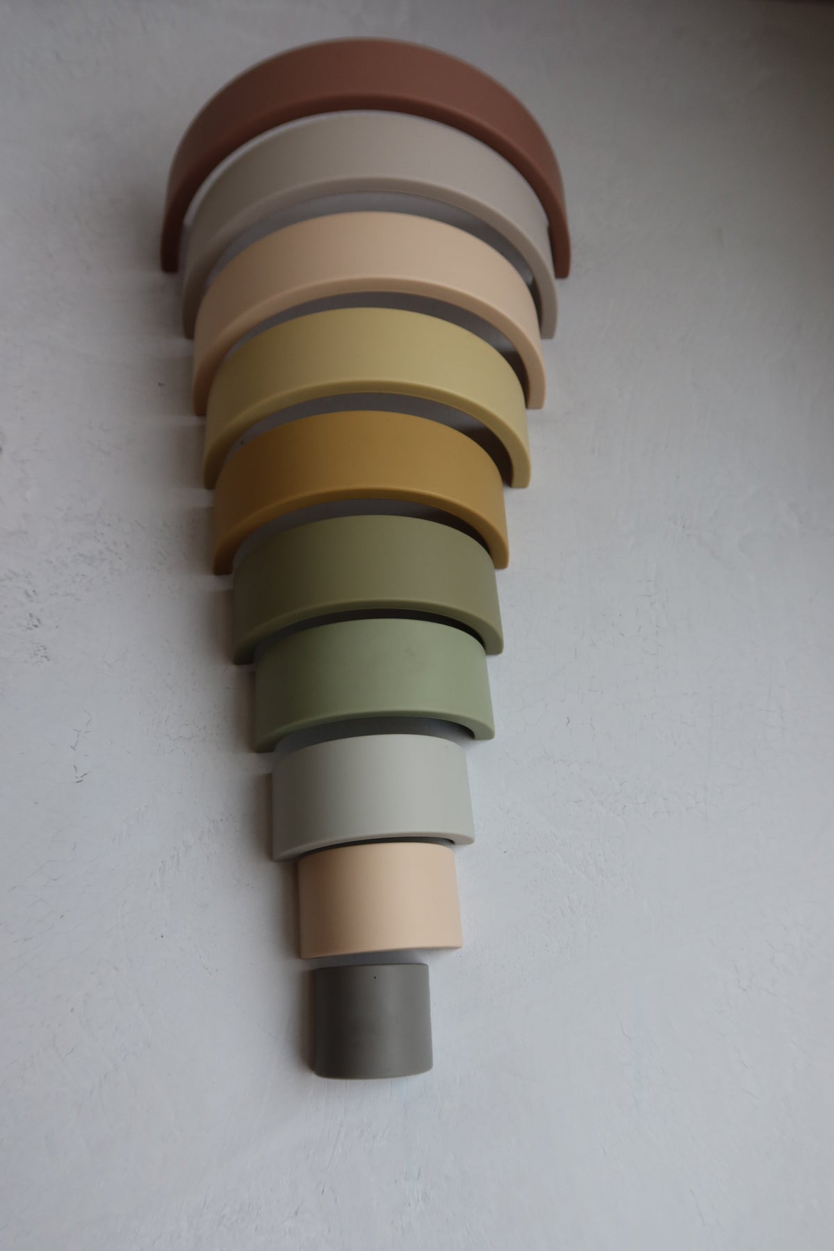 Silicone Rainbow Stacking Toy (10 pc) featuring ten nested silicone arches in descending sizes and varying muted colors.