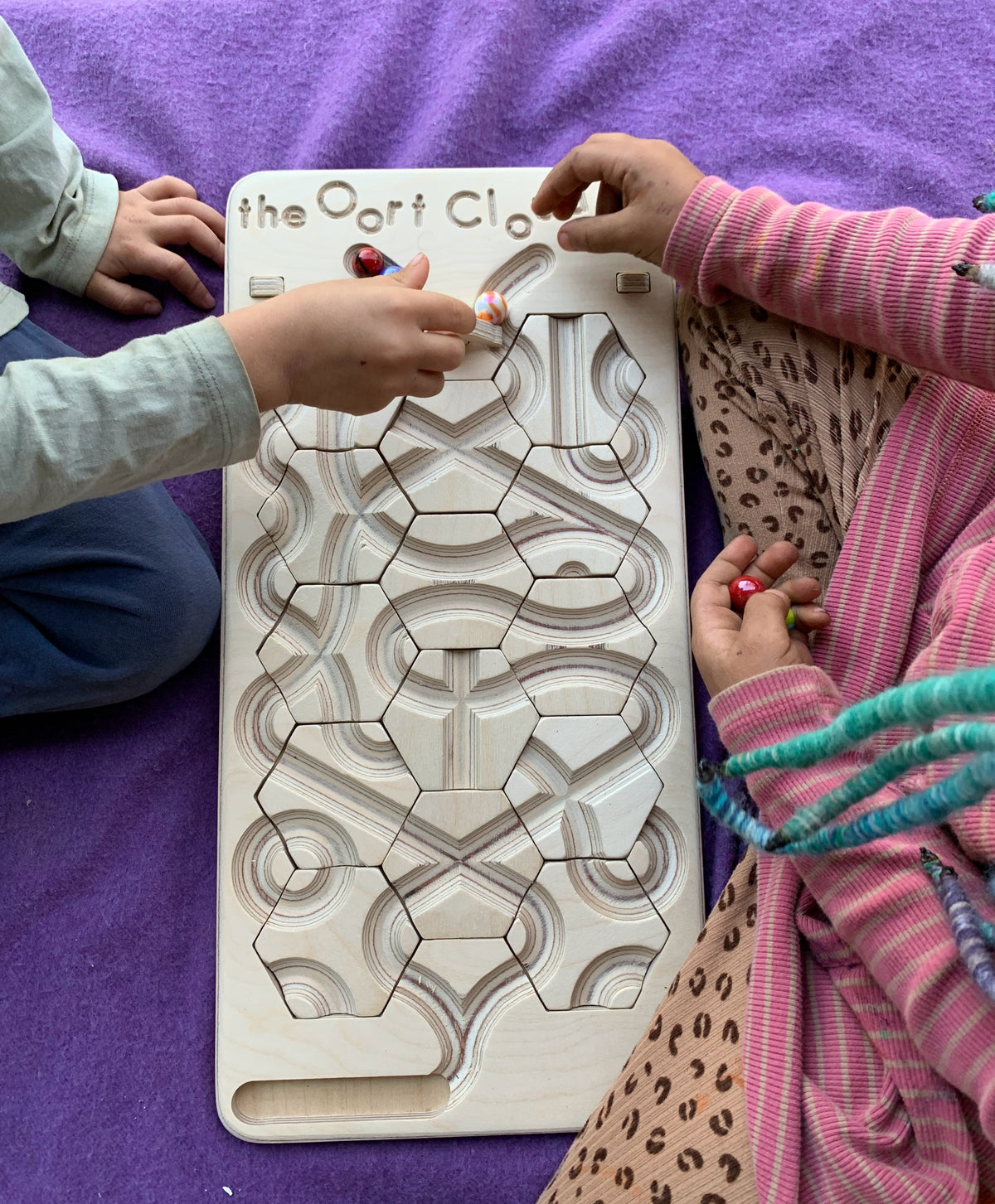 Two children playing with The Oort Cloud – Wooden Marble Run Puzzle on a purple blanket.